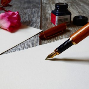 A romantic setup with a rose, fountain pen, and paper, perfect for heartfelt writing.